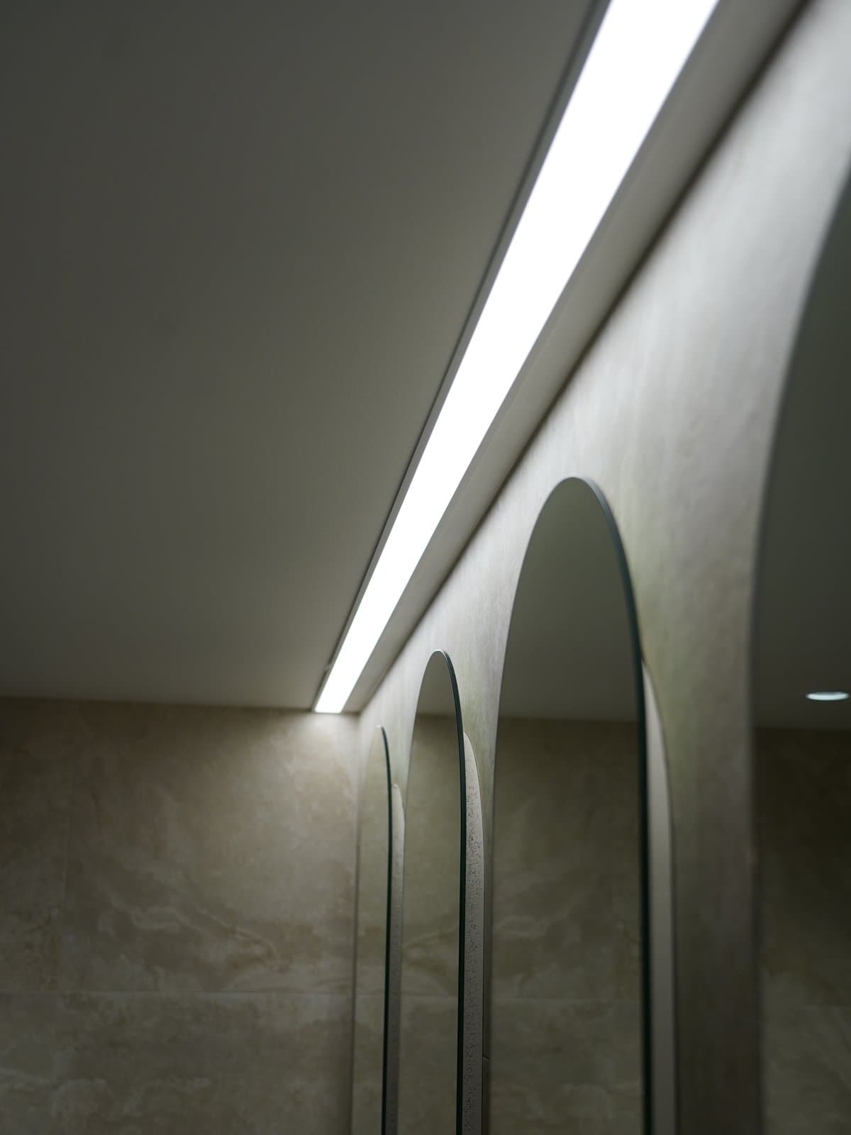 Arched mirrors and a light strip along a bathroom ceiling