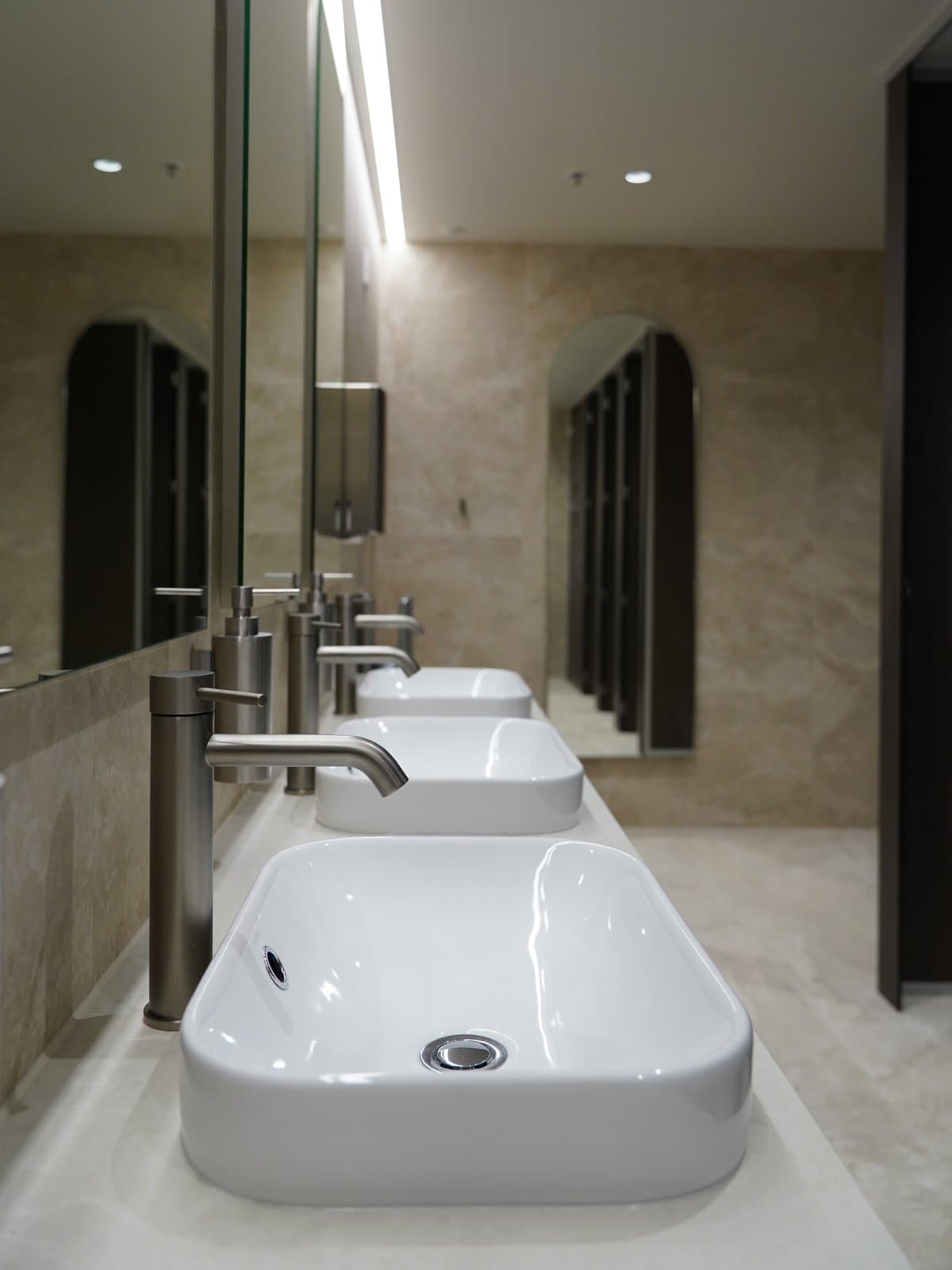 A row of modern sink basins beneath arched mirrors